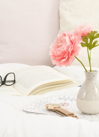 God Loves Me - Marva Smith - flowers in vase on a bed with glasses and book.